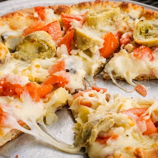 A partially eaten pizza with artichokes, tomatoes, and melted cheese on a metal pan.