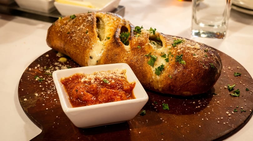 Golden-brown cheesy bread with herbs and parmesan, served with a side of marinara sauce on a wooden board.