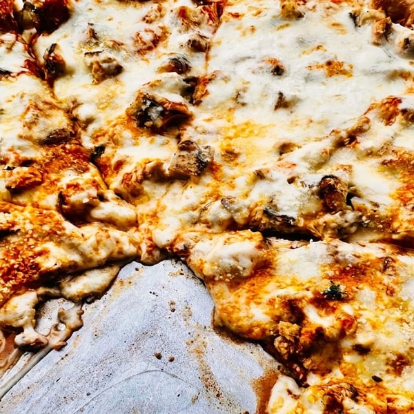 Close-up of a freshly baked pizza with melted cheese and a missing slice on a metal tray.