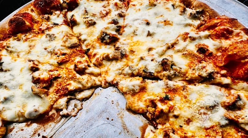 Close-up of a freshly baked pizza with melted cheese, chicken, and a missing slice.