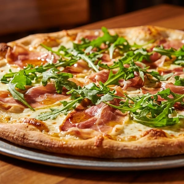 A whole pizza with prosciutto, arugula, and cheese on a metal tray on a wooden table.