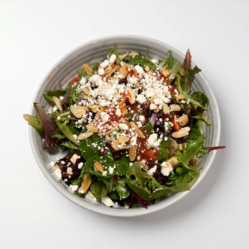 A vibrant salad with mixed greens, feta cheese, sliced almonds, and a red dressing in a gray bowl.